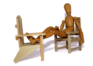 Immagine di un manichino di legno seduto e con piedi appoggiati, su sedie di legno